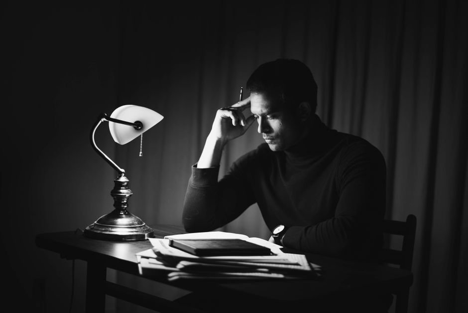 Banker Who Once Owned America — Black and white thoughtful young male in dark clothes reading book while sitting at desk with