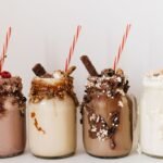 From Milkshake Salesman to Global — Close-up of four assorted milkshakes with various toppings in glass jars.