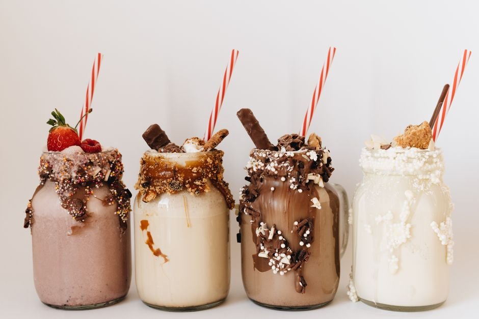 From Milkshake Salesman to Global — Close-up of four assorted milkshakes with various toppings in glass jars.