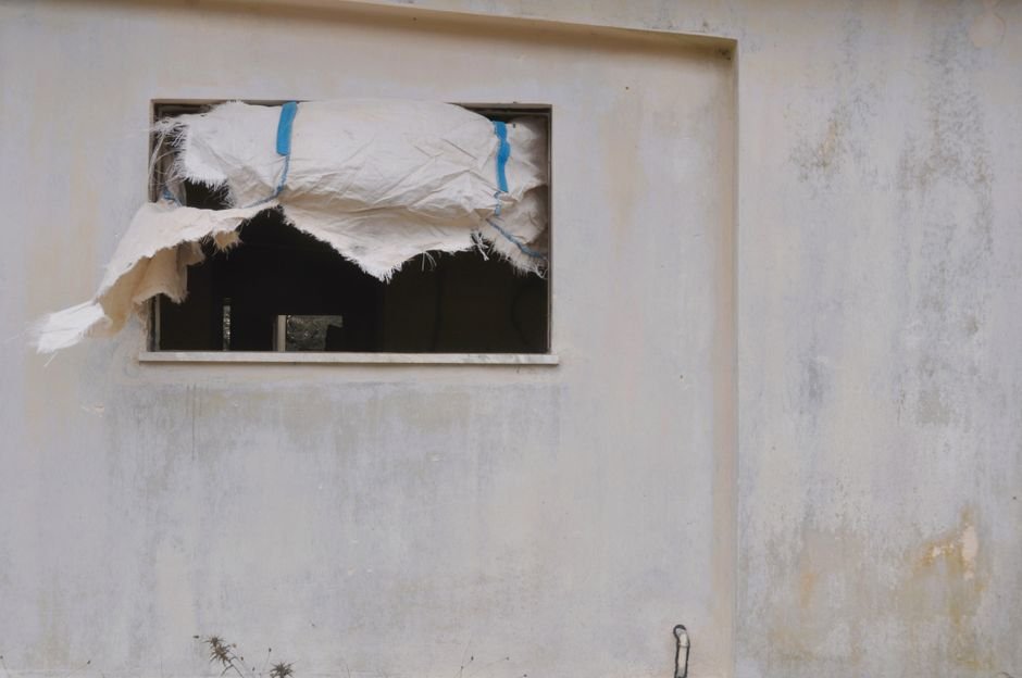 From Rags to Steel — A window with torn fabric exposing the interior of an abandoned building.