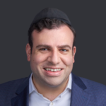 Lehman — Portrait of a smiling man wearing a suit and kippah on a dark background.