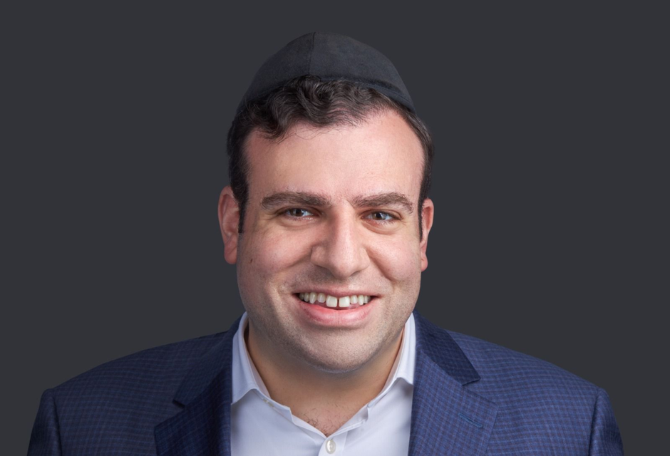 Lehman — Portrait of a smiling man wearing a suit and kippah on a dark background.