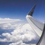 Pan Am Vanished From the Skies — View from airplane window showcasing a wing above fluffy clouds during daylight.