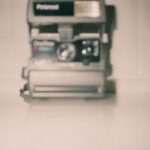 Polaroid Fell Twice After Instant Glory — Blurred vintage Polaroid camera on a white surface creating a nostalgic feel.