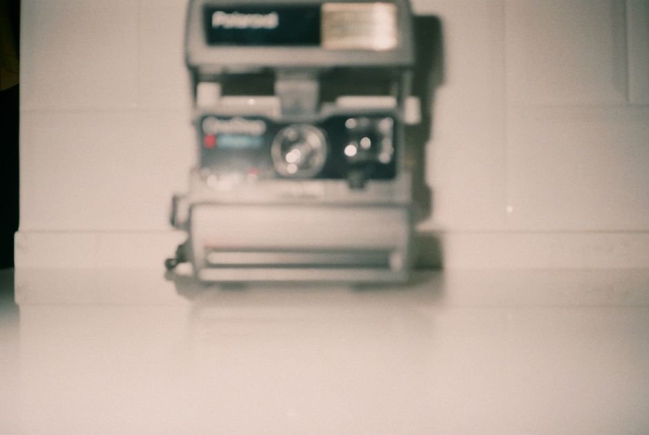 Polaroid Fell Twice After Instant Glory — Blurred vintage Polaroid camera on a white surface creating a nostalgic feel.