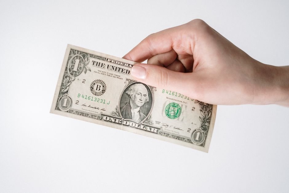 Quiet Power of Dollar‑Cost Averaging — Close-up of a Caucasian hand holding a US one dollar bill against a white background.