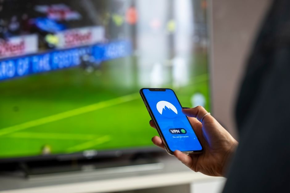 Streaming Wars Are Quietly Bankrupting Giants — Close-up of a person holding a smartphone with a VPN app, streaming sports on