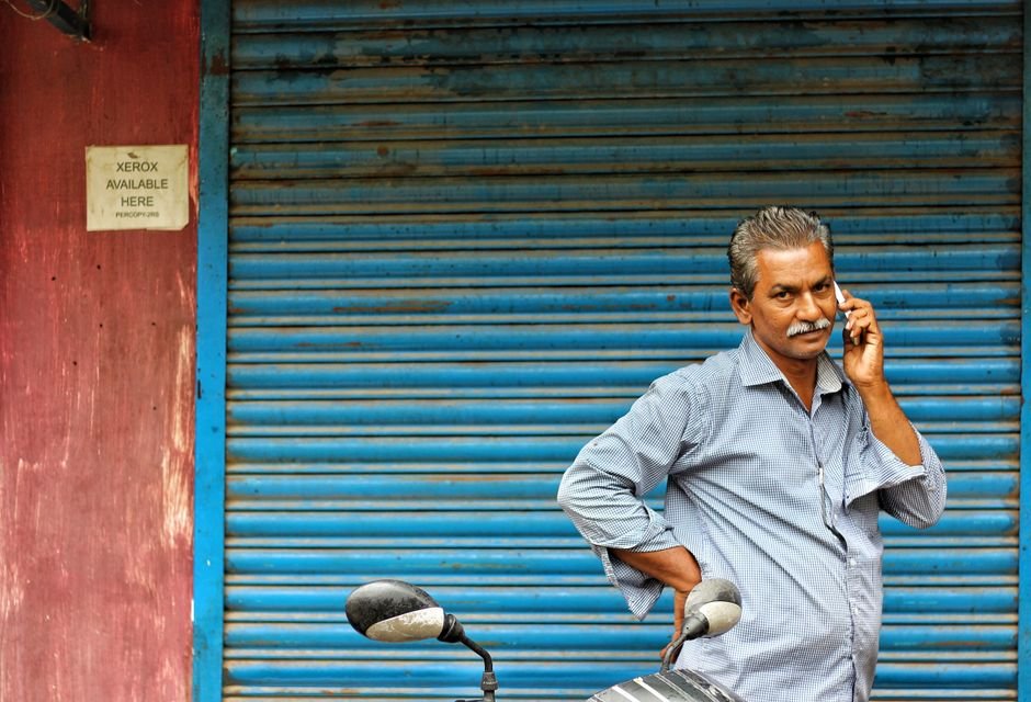 Xerox — Middle-aged man on phone stands by closed shop shutter, mirror visible.