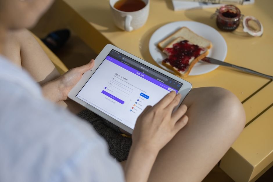 Yahoo — A woman using a tablet while having a snack with jam on toast and tea, reflecting a cozy indoor setting.
