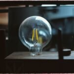 the Phoebus Cartel Engineered Light‑Bulb Death — A detailed close-up of a traditional light bulb placed on a workbench in a w